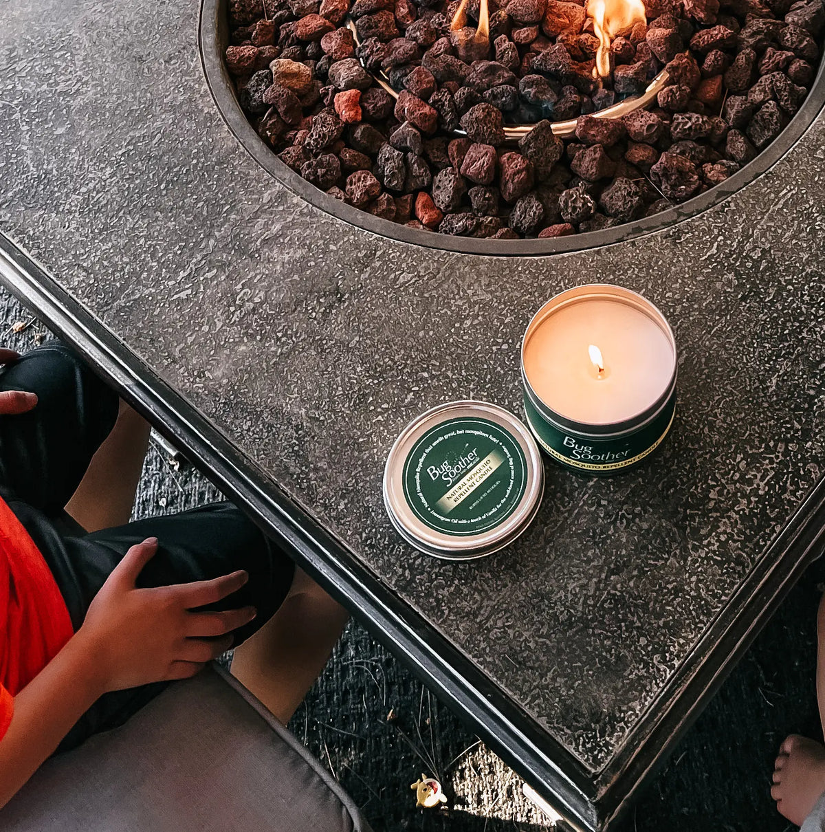 Top view of lit Bug Soother candle on the edge of a firepit. 