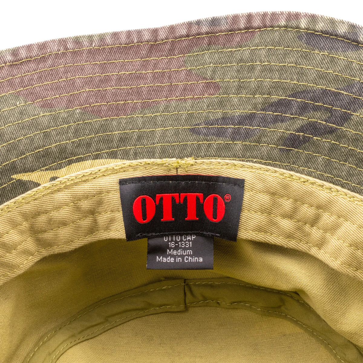 Close-up of the inside of a camouflage cap showing the black brand label with red 'OTTO' text and size details.