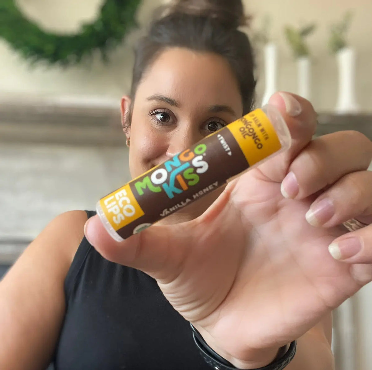 A woman holding up a Mongo Kiss Vanilla Honey lip balm. 